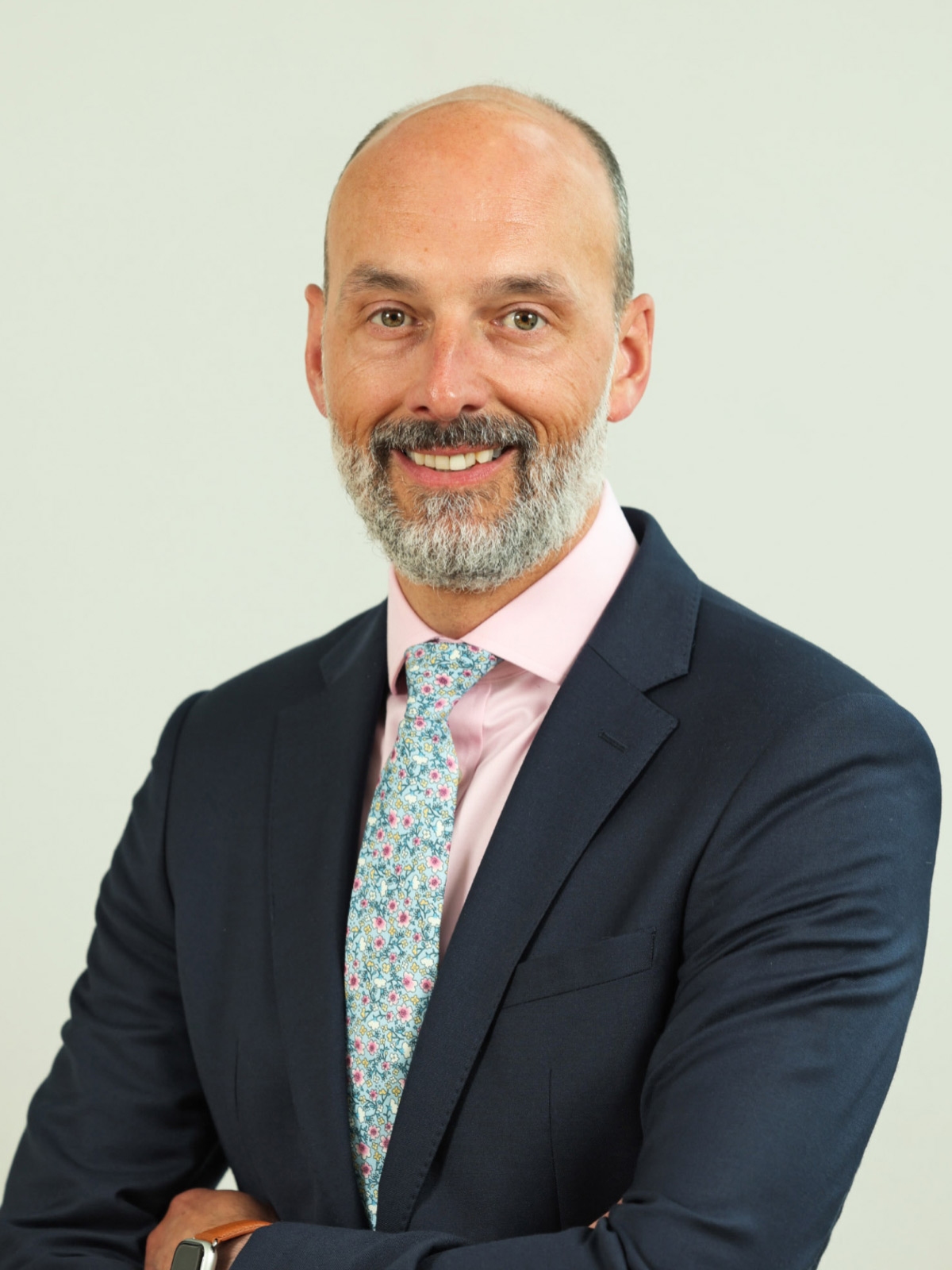 gentleman with navy suit, pink shirt, green and white floral tie and grey hair and beard